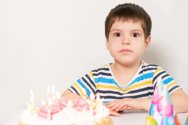 Un chico guapo celebra un cumpleaños, se sienta en una mesa con un pastel con tamices ardientes, un lugar para el texto. — Foto de Stock