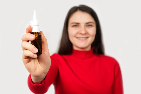 Une femme brune en rouge montre une bouteille de spray nasal pour traiter la rhinite et les allergies — Photo