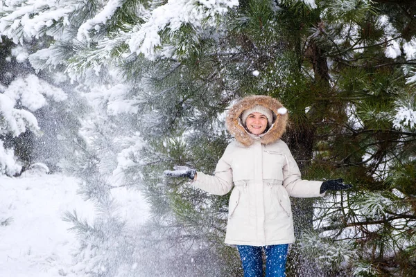 Una donna in una foresta innevata invernale sorride guardando la macchina fotografica, i fiocchi di neve volano. — Foto Stock