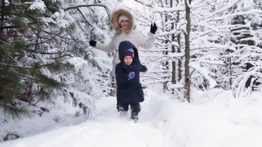 Anne ve oğlu karlı bir kış ormanında koşuyorlar, mutlu ebeveynlik ve aile tatili, yavaş çekim.