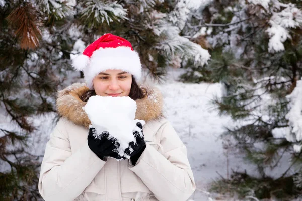 A woman in Santas hat holds a snowball in her hands in a snow-covered winter forest, a place for text — Photo