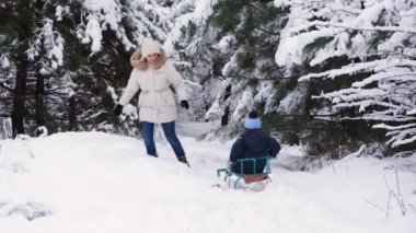Bir anne kışın karla kaplı bir ormanda kayak merkezinde oğlunu kızağa çeker.