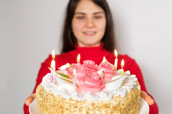 Una morena vestida de rojo sostiene un gran pastel blanco con velas, pide un deseo —  Fotos de Stock