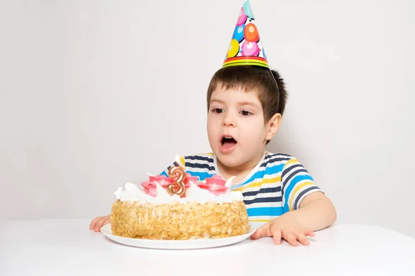 Un niño con una gorra festiva apaga las velas del pastel en su cumpleaños —  Fotos de Stock