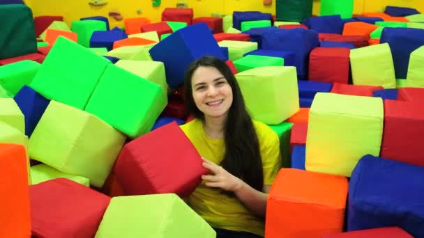 Beautiful brunette woman sitting in a childrens playroom in a pool with soft large cubes and smiling, slow motion shooting. — Stock Video