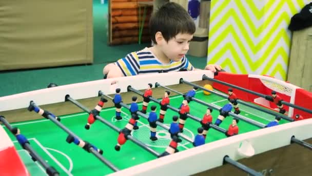 Ein 4-jähriger Junge spielt Tischkicker im Kinderspielzimmer. — Stockvideo