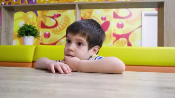 Um garotinho de 4 anos se senta em uma mesa em um café, aponta o dedo para o lado e diz. — Vídeo de Stock