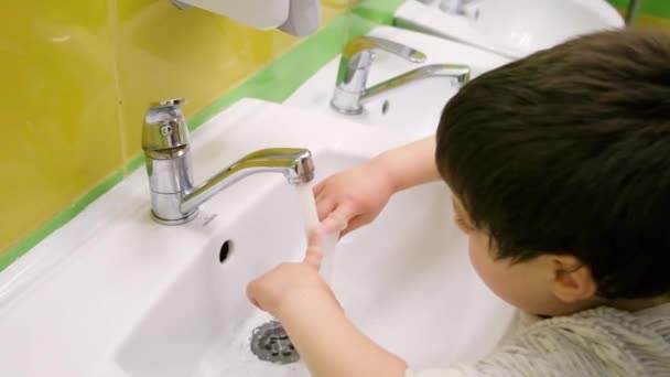 Um menino de 4 anos lava as mãos sob uma torneira por conta própria — Vídeo de Stock