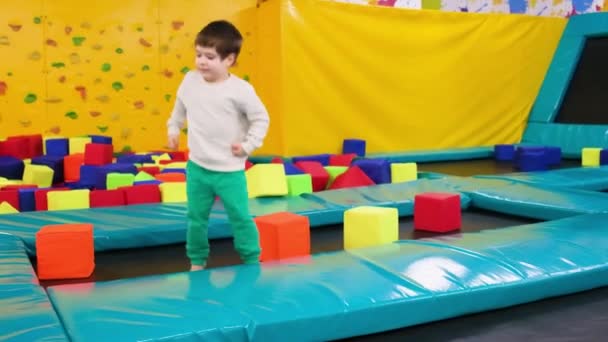 一个漂亮的学龄前儿童跳到蹦床上，在游戏室里玩得很开心 — 图库视频影像
