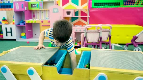 Um menino pré-escolar desempenha um conjunto de construção em uma sala de jogos para crianças — Vídeo de Stock