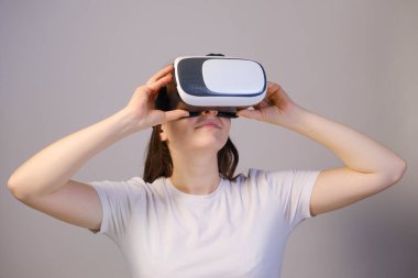 Sanal gerçeklik gözlüklü bir kadın gri bir arka plana bakıyor..