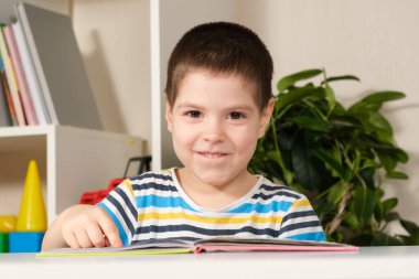 4 yaşında güzel, mutlu bir çocuk okumayı öğrenir, bir kitabın önünde oturur, kameraya bakar ve gülümser.