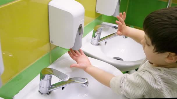 Un niño en edad preescolar pone su mano bajo un dispensador de jabón, se lava las manos y se lava las manos con agua — Vídeo de stock