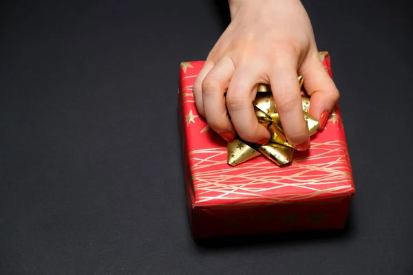 A női kéz megragad egy ajándék dobozt egy íj egy fekete háttér egy hely a szöveges. — Stock Fotó