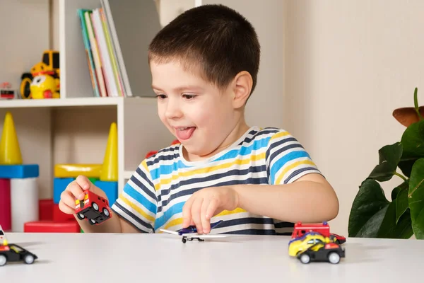 El niño juega con los coches, está fascinado por el juego y saca la lengua. — Foto de Stock