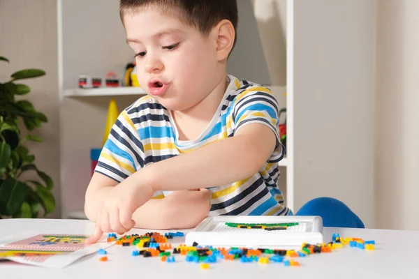 Un niño de 4 años juega con un mosaico, recoge una imagen de pequeñas piezas de plástico. Desarrollo de habilidades motoras finas en niños — Foto de Stock