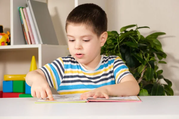 Щасливий хлопчик 4 років дивиться на книгу з малюнками, показує фотографії і називає їх . — стокове фото