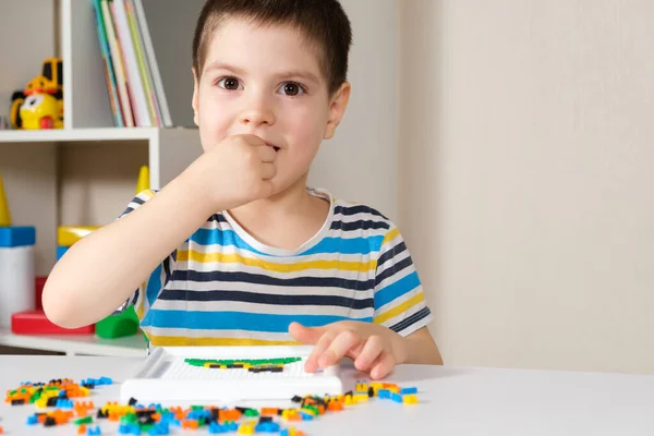 A criança brinca com mosaicos, pequenos objetos para crianças, leva um pequeno detalhe do mosaico em sua boca. Perigo de engolir uma parte. — Fotografia de Stock