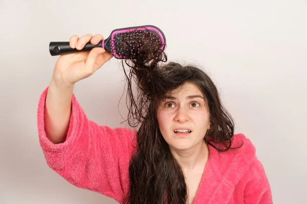 Una mujer trata de peinarse el cabello enredado y húmedo. Cuidado del cabello en casa, caída del cabello y sección. — Foto de Stock