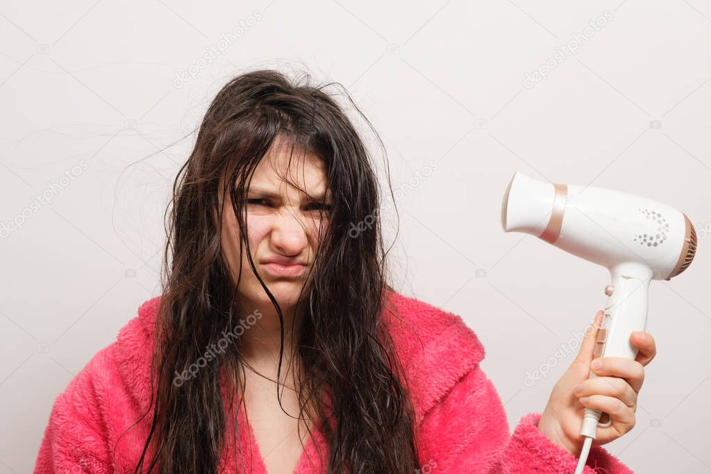 A brunette woman with matted hair dries it with a hair dryer. Hair care, overdried hair