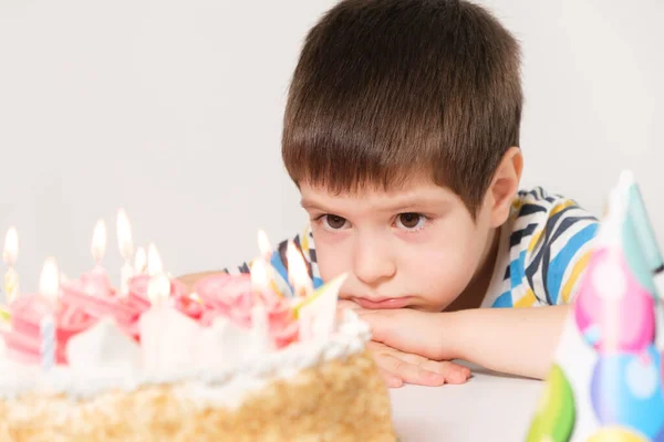 Un chico guapo celebra un cumpleaños, se sienta frente a un pastel con velas y pide un deseo — Foto de Stock