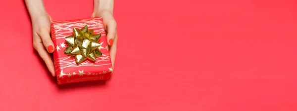Női kéz piros manikűr tart egy ajándék doboz piros alapon helyet a szöveges. — Stock Fotó