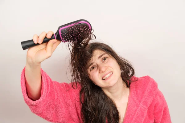 Una mujer trata de peinarse el cabello enredado y húmedo. Cuidado del cabello en casa, caída del cabello y sección. — Foto de Stock