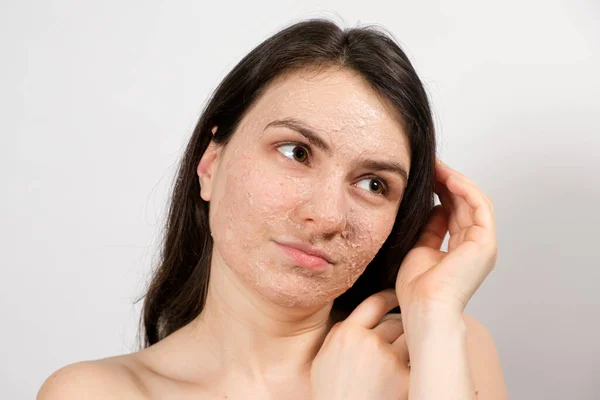 Seorang wanita muda yang cantik mengoleskan scrub atau masker ke wajahnya, perawatan kulit wajah, pembersihan kulit — Stok Foto