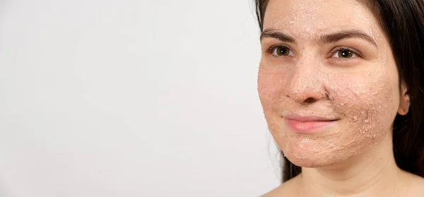 Een jonge brunette vrouw maakt reinigende gezichtsbehandelingen - een masker of scrub om de huid te reinigen en te voeden, banner met plaats voor tekst. — Stockfoto
