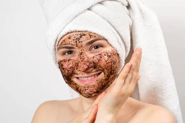 Una joven con una máscara de café en la cara y una toalla de baño en la cabeza sonríe y mira a la cámara sobre un fondo blanco. —  Fotos de Stock