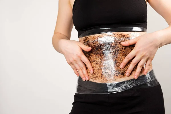 A woman makes a belly wrap with a coffee anti-cellulite body scrub. The concept of weight loss and skin care — Stock Photo, Image