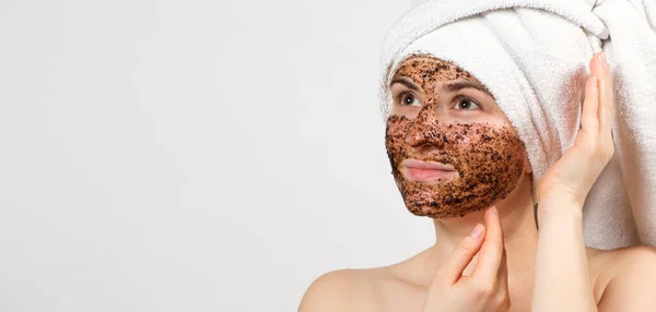 Una hermosa joven con una toalla de baño en la cabeza y una máscara de café en la cara cuida su piel, una pancarta con espacio para el texto —  Fotos de Stock