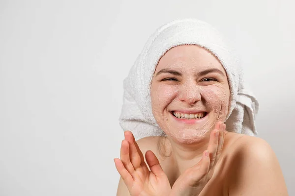 Een jonge glimlachende vrouw met een natuurlijk masker of ubtan op haar gezicht en een witte handdoek op haar hoofd, een plek om te sms 'en, ruimte kopiëren — Stockfoto