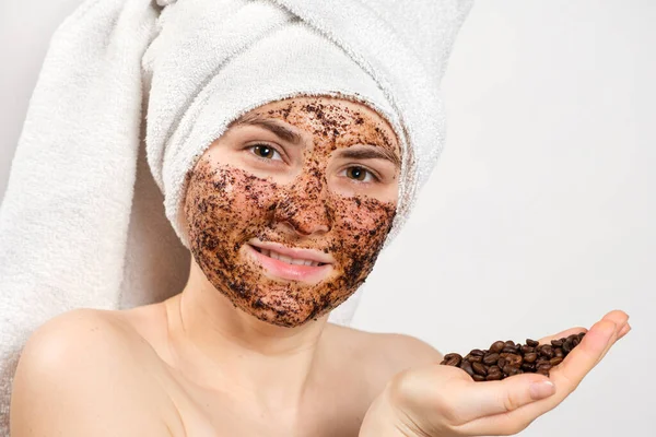 Жінка з кавовою маскою або скрабом на обличчі тримає в руці жменьку кавових зерен — стокове фото