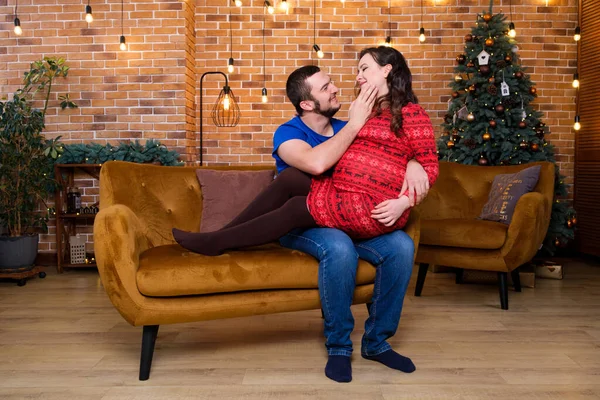 Mutlu anne babalar kanepeye oturur ve güler, hamilelik ve noel.