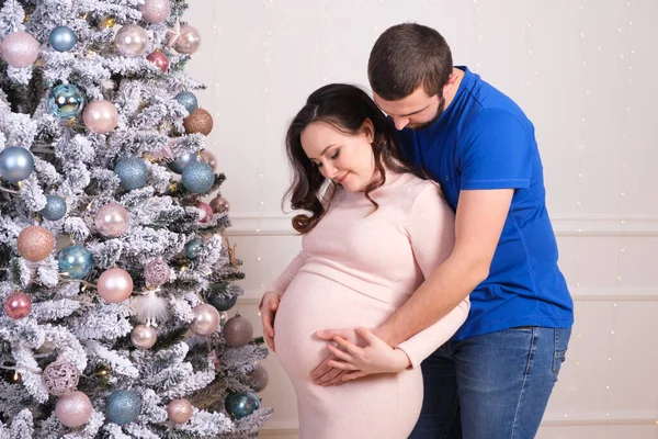 Mari et femme profitent de la grossesse ensemble, debout près du sapin de Noël. Joyeux bébé attendre et Noël — Photo