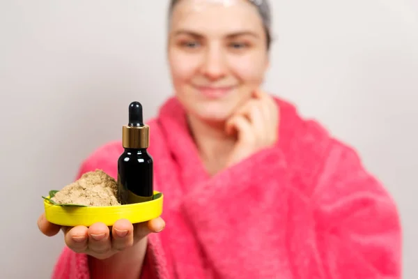 Una mujer guarda cosméticos naturales para el cuidado del cabello - una botella de aceites y ubtan, un exfoliante de hierbas —  Fotos de Stock