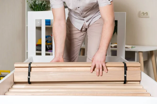 Een mannelijke meubelmaker legt houten latten op een nieuw wit bed — Stockfoto