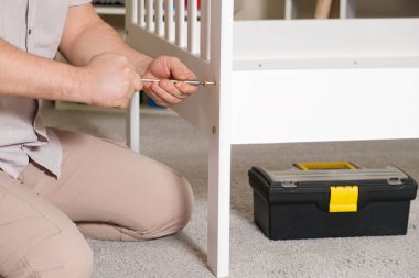 Mobilya derleyicisi yatağı monte eder, vidaları ahşap parçalara çevirir, elleri yakın çekim tornavidayla çevirir.