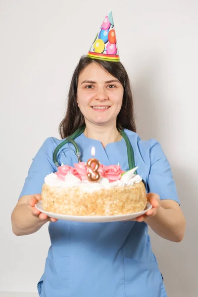 El médico o enfermero sostiene un pastel de cumpleaños con el número tres para el aniversario de la apertura de la clínica —  Fotos de Stock