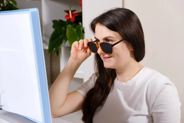 A woman looks at a computer screen through perforated glasses with holes to improve vision in astigmatism and keratoconus — Stock Photo, Image