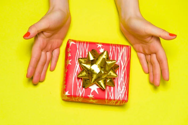 Gyönyörű piros ajándék doboz íj a nők kezében a sárga háttér, felülnézet, másolás helyet szöveg. — Stock Fotó