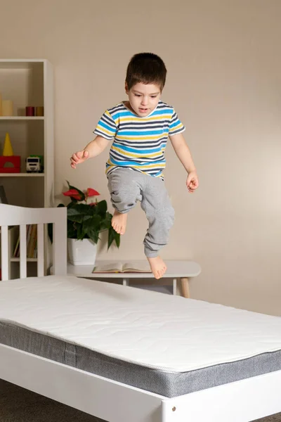 Un niño guapo de 4-5 años salta sobre una cama de madera sobre un colchón, foto vertical —  Fotos de Stock