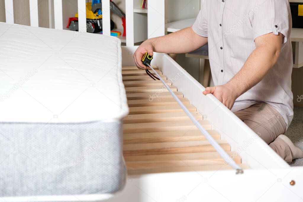 A man assembles a childrens bed, measures the length with a tape measure, hands close-up.