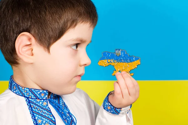 Ребенок в вышитой рубашке на фоне флага держит в руках карту Украины, место для текста. — стоковое фото