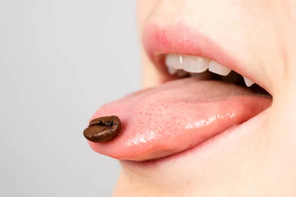 Eine Kaffeebohne auf der Zunge im Mund. Liebe zum Kaffee, Sucht, Kaffeewahn. Platz für Text, Kopierraum für Banner — Stockfoto