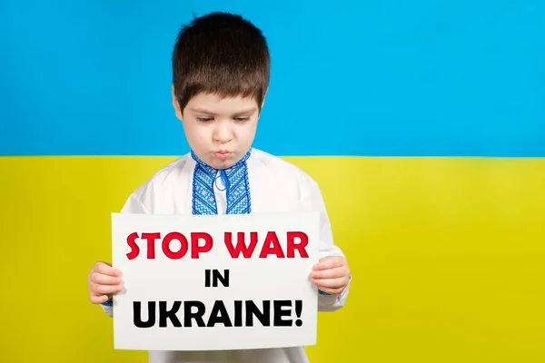 Украинский мальчик 4 лет держит лист с текстом Stop War в Украине. На фоне сине-желтого флага есть место для текста. — стоковое фото