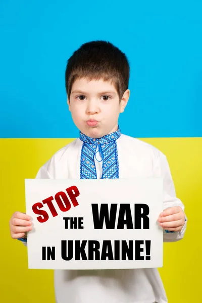 Украинский мальчик 4 лет держит лист с текстом Stop the War in Ukraine, на фоне сине-желтого флага. — стоковое фото