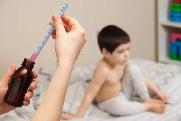 De kinderarts of moeder typt in een maatspuit het geneesmiddel voor hoest of temperatuursiroop voor het kind — Stockfoto