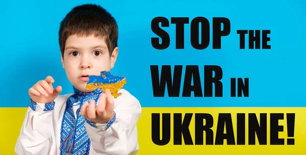 Украинский мальчик в национальной одежде держит в руках карту Украины, баннер с текстом Stop the War in Ukraine. — стоковое фото